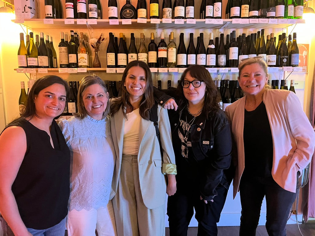 Five women posing together in front of a wine shelf