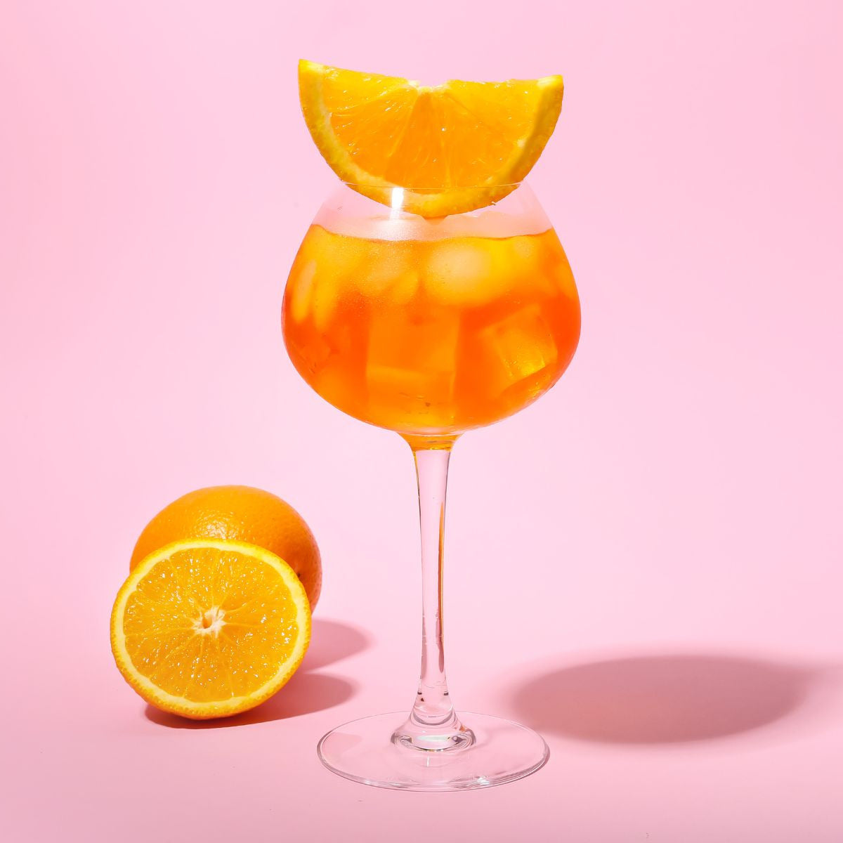 Orange cocktail in a glass with an orange slice on a pink background