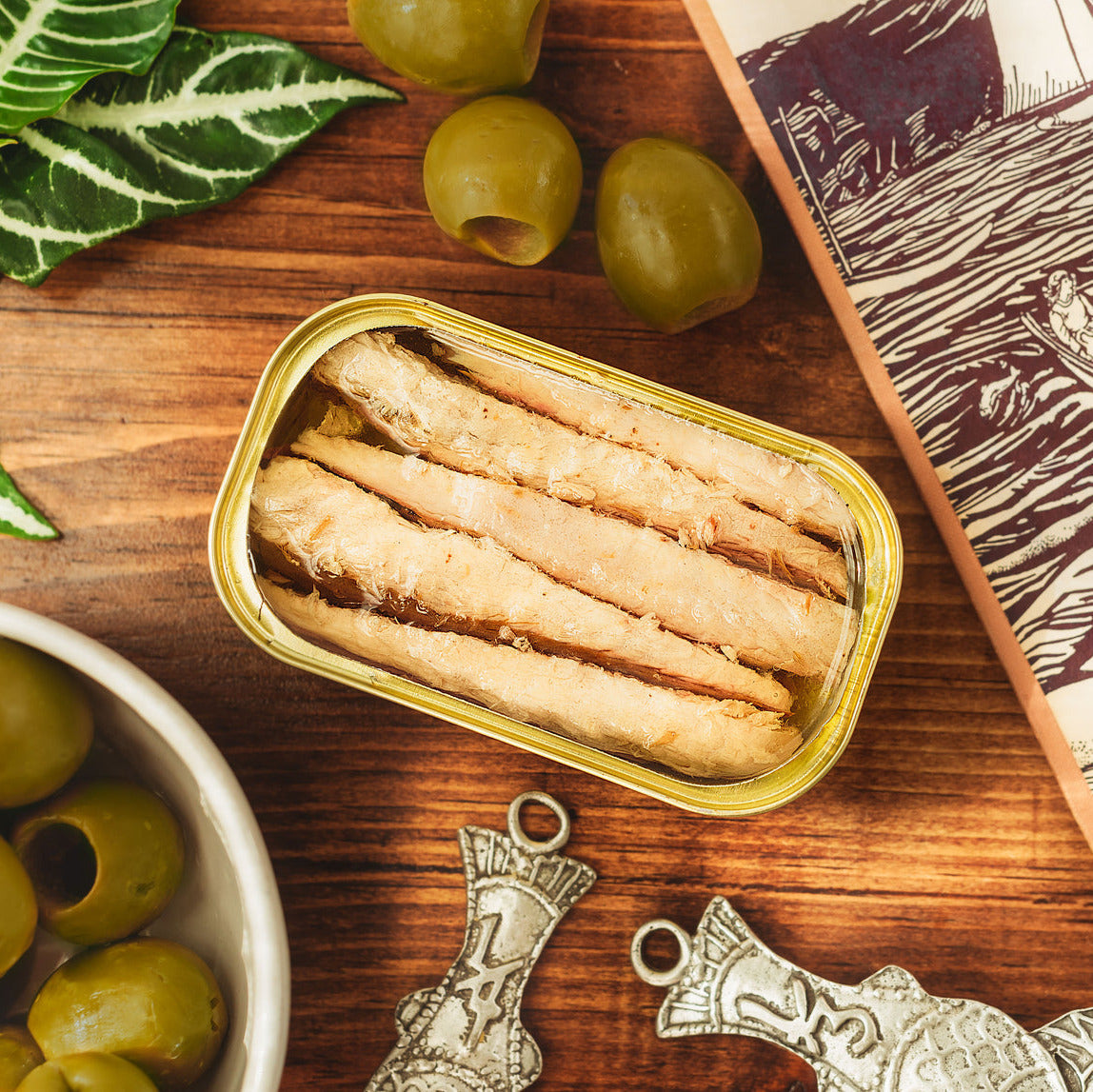 Mackerel Fillets in olive oil on a wooden table surrounded by olives