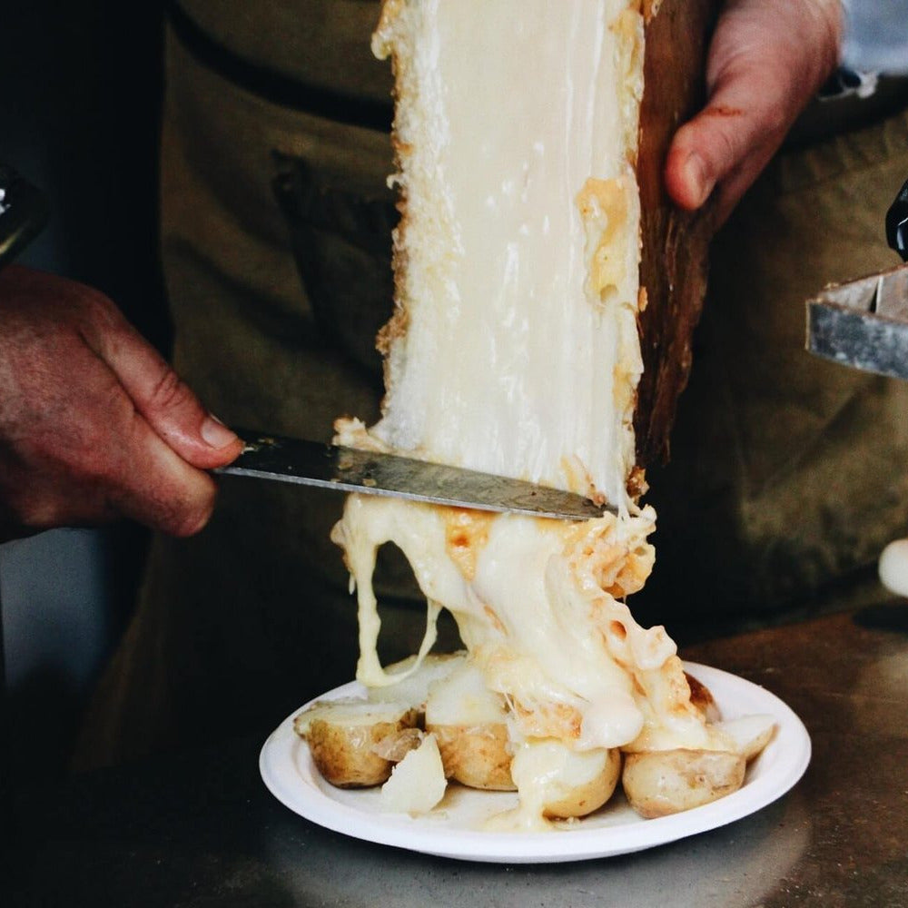 Person cutting a large block of cheese with a knife over a plate of bread.