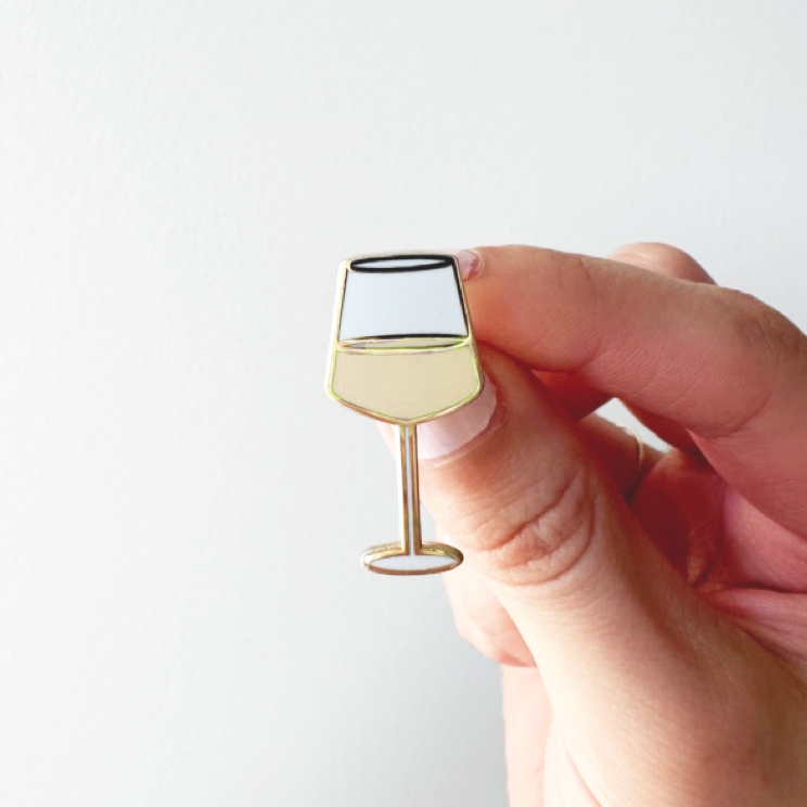 Hand holding a small wine glass-shaped pin against a white background