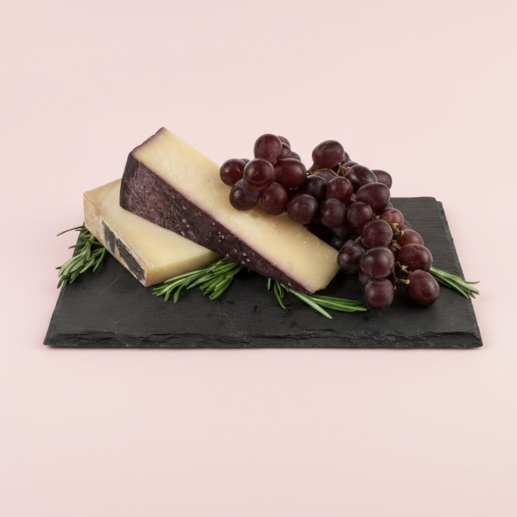 Two pieces of cheese and a bunch of grapes on a black slate board with rosemary leaves.