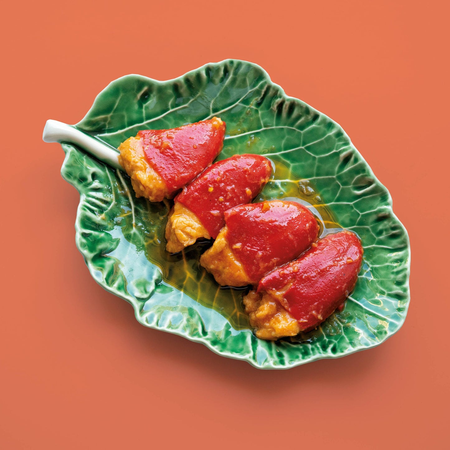 Green leaf-shaped plate with stuffed red peppers on an orange background