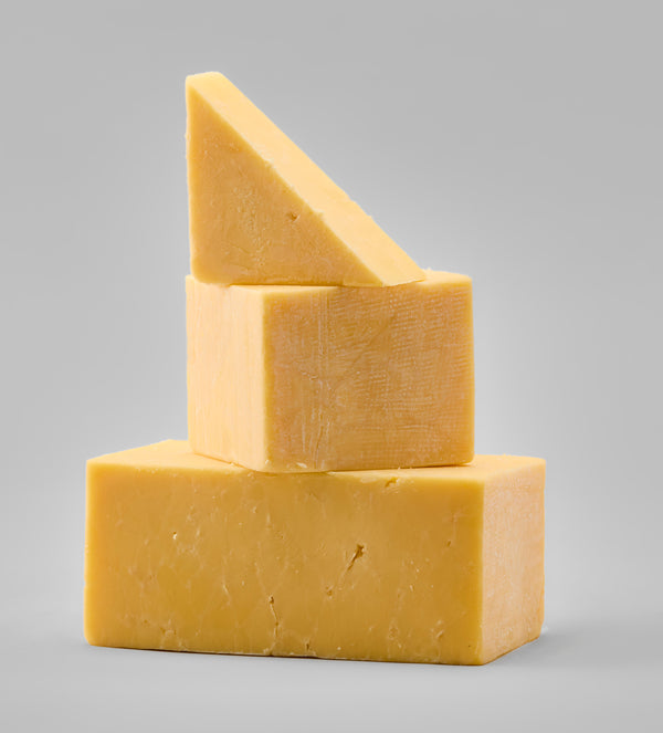 Three stacked blocks of yellow cheese on a light gray studio background.